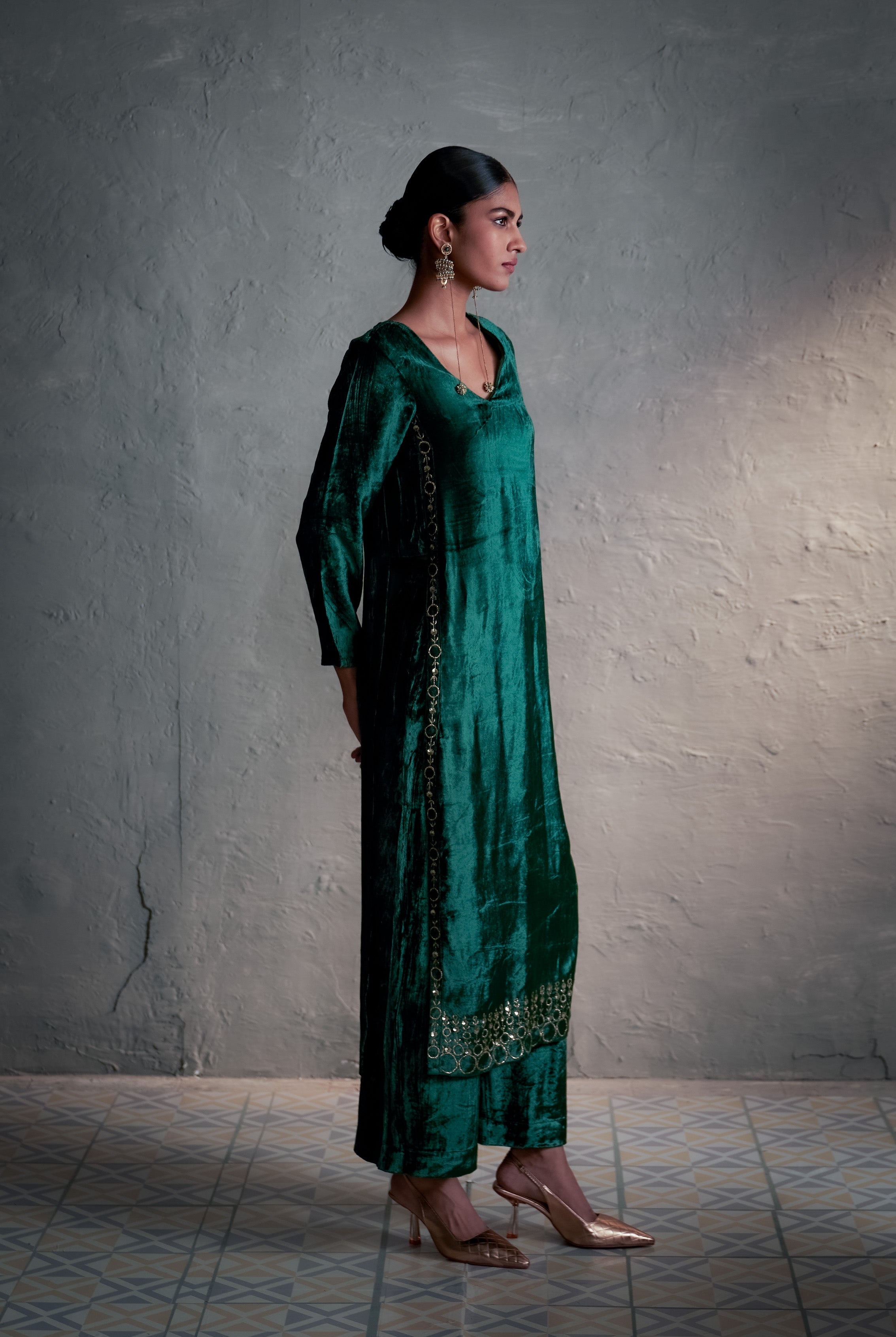 Woman wearing a green traditional outfit against a textured wall.