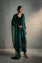 Woman wearing a green traditional outfit against a gray wall.